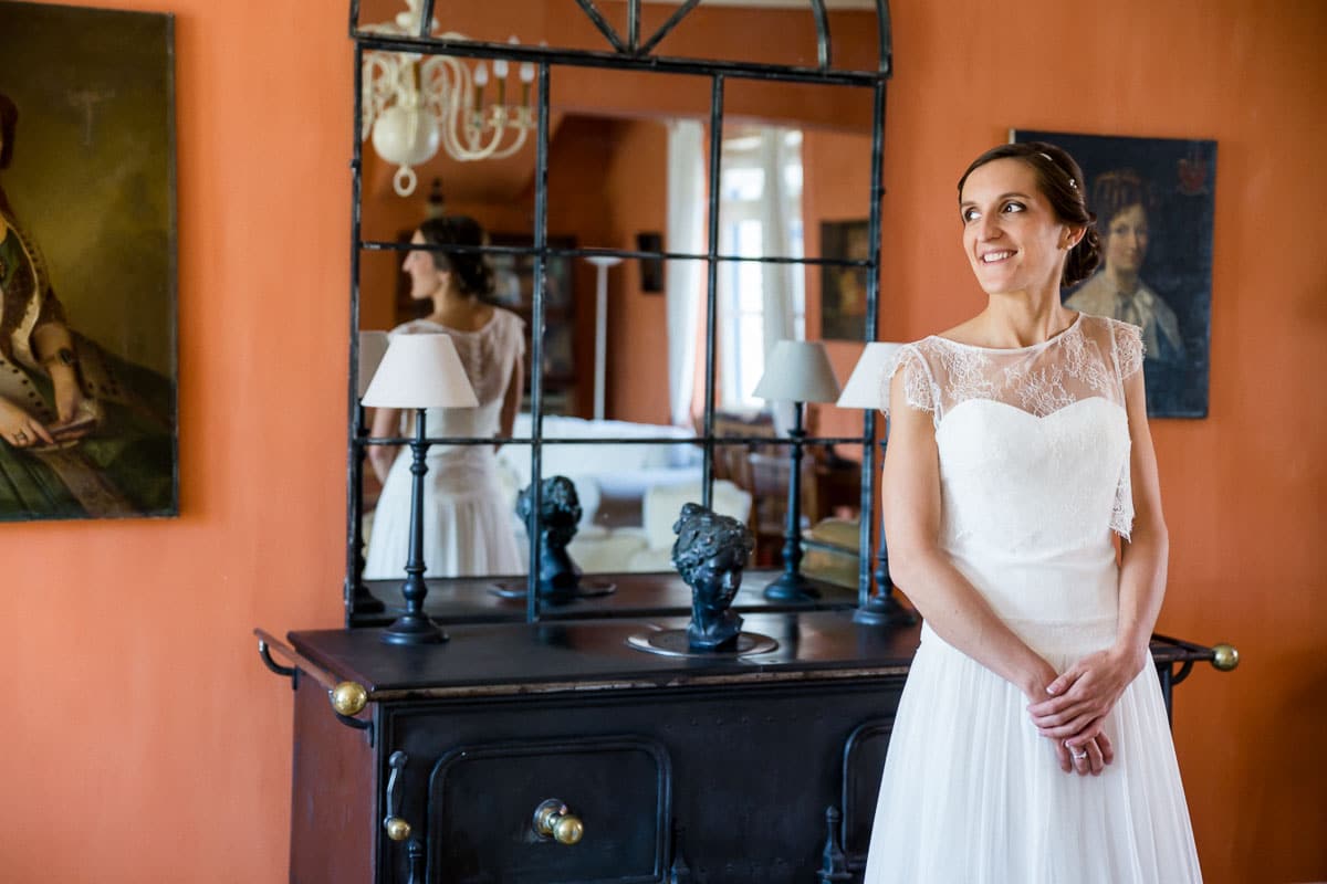Mariée en robe de mariée souriante devant un grand miroir lors de ses préparatifs dans le nord