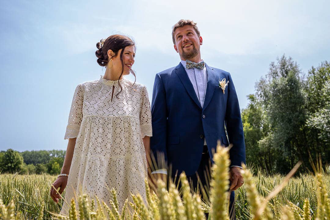 Couple de mariés au milieu d’un champs de blé vert lors d’une séance de couple à Douai.