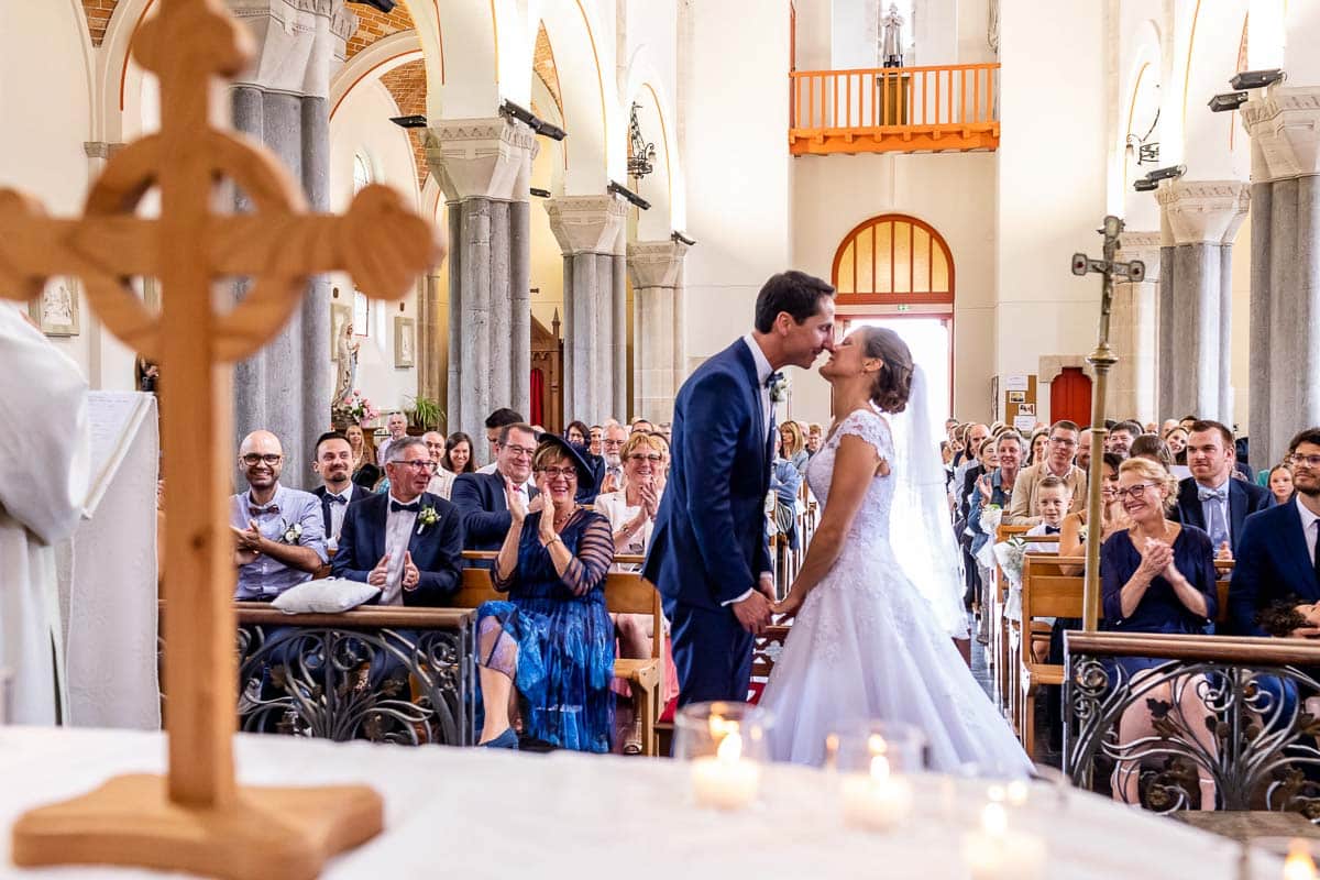 Couple de mariés qui s’embrassent dans une église dans le nord, à l’arrière plan on aperçoit les invités qui applaudissent