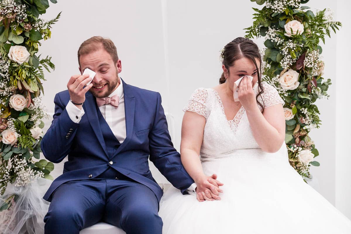 Mariés assis qui se tiennent la main, dans l’autre main ils tiennent un mouchoir et essuient leurs larmes