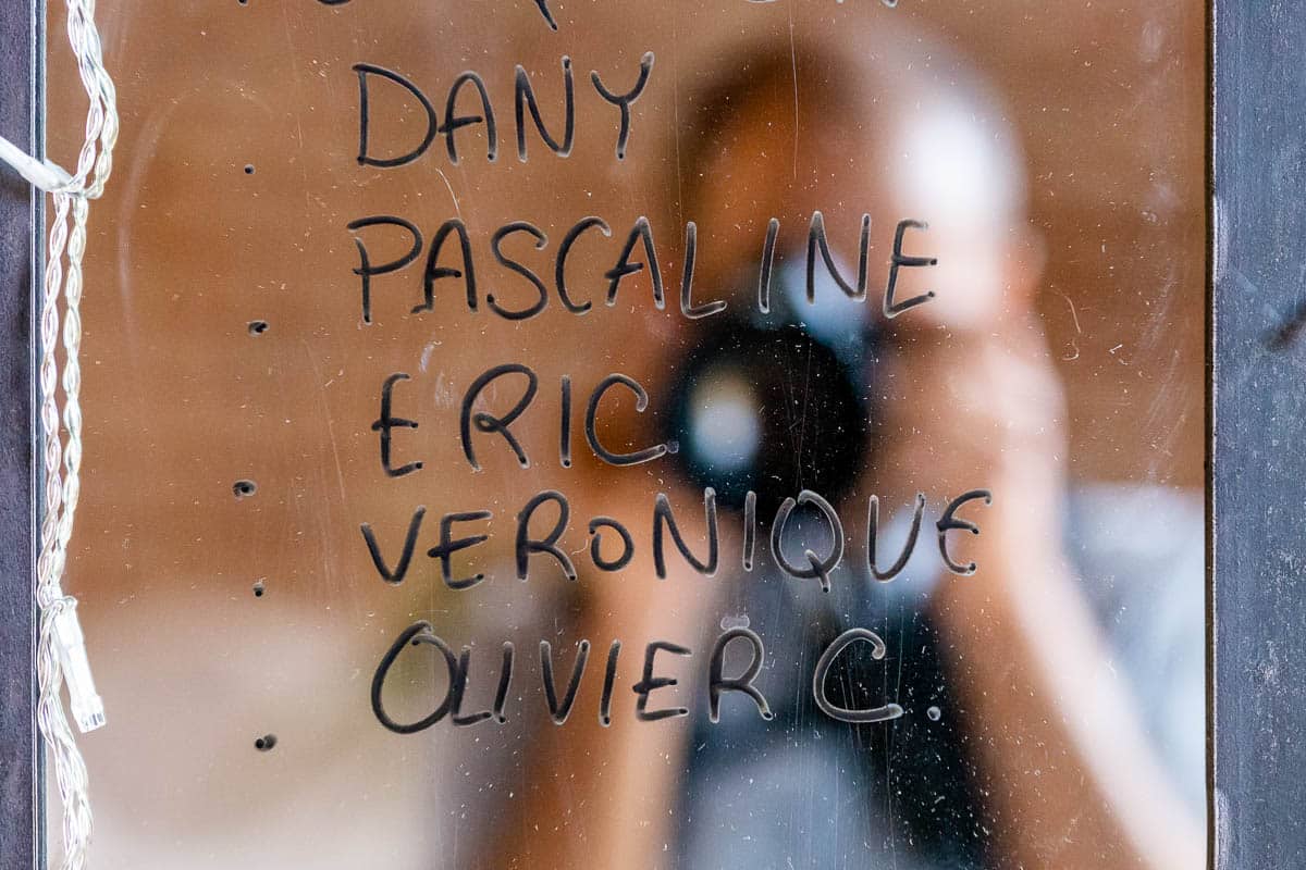 Autoportrait flou d’Olivier Cousson photographe dans le reflet d’un miroir. Le miroir représente le plan de table et son prénom est écrit dessus