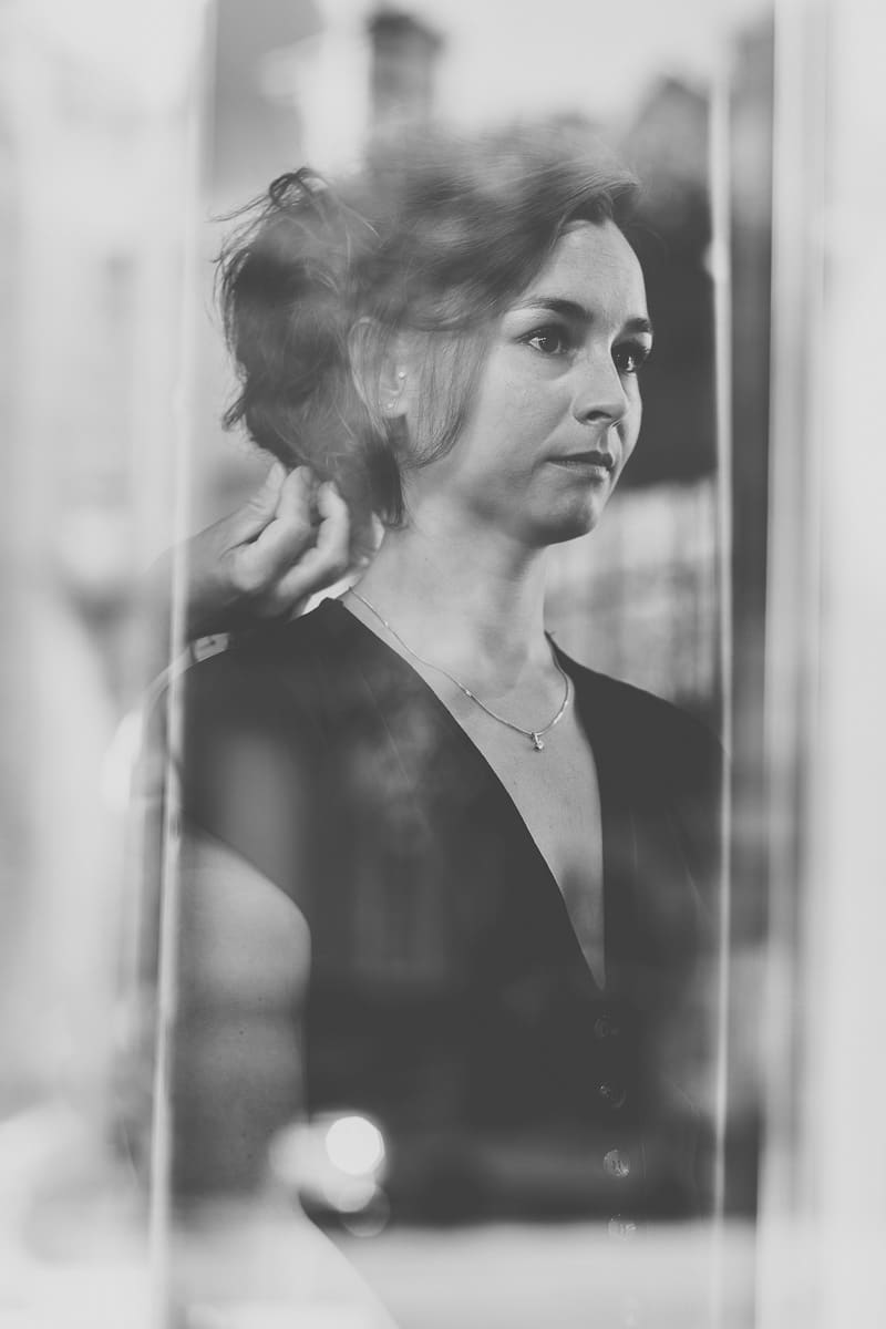 Portrait en noir et blanc d’une mariée à travers une vitre lors des préparatifs d’un mariage à Boulogne-sur-Mer