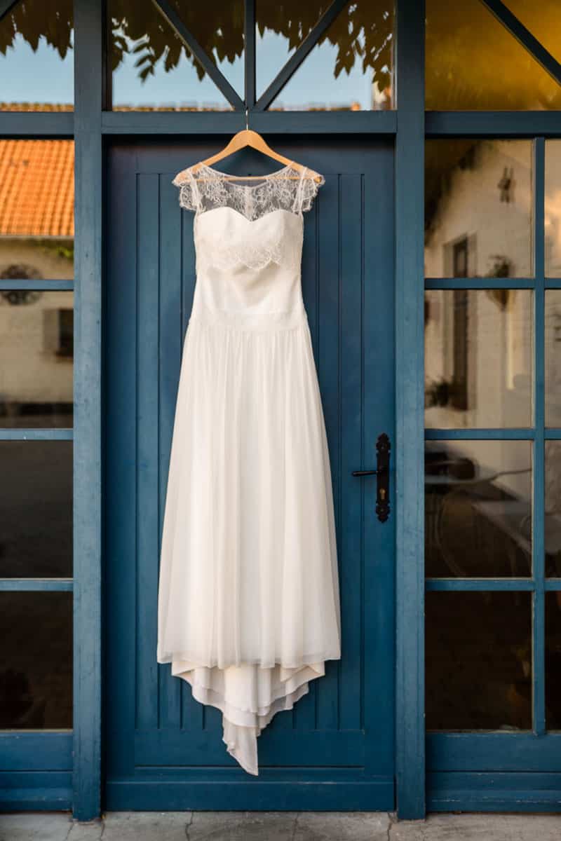 Gros plan d’une robe de mariée accrochée à une porte bleue lors des préparatifs